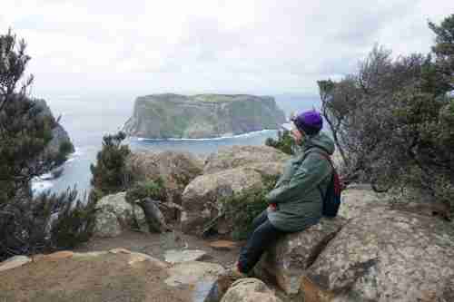 solo travel Tasmania sitting on a rock enjoying the island and water views on the three capes track, the perfect hike for a 10 days in Tasmania itinerary