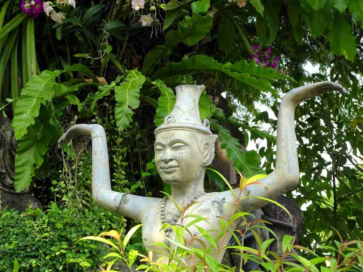 Thai statue in a lush green tropical garden at the Grand Palace in Bangkok