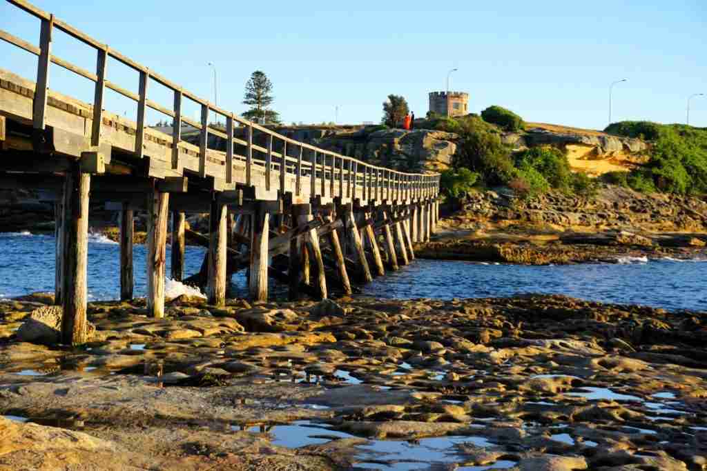 A wooden bridge on an ocean rock platform that joins Bare Island in La Perouse to the  headland