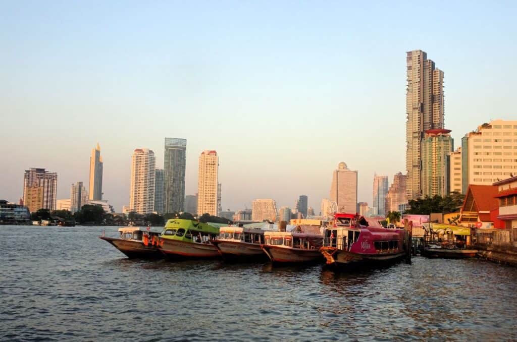 Boats moored on the Chao Phraya River in Bangkok with tall buildings behind