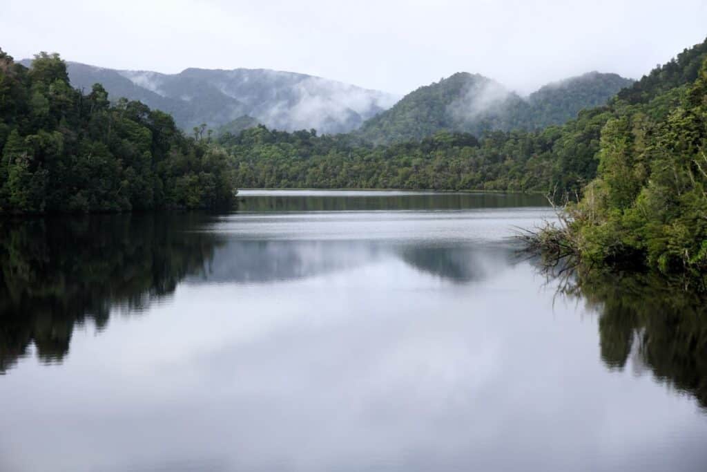 the still ness of the Gordon River surrounded by misty forested mountains