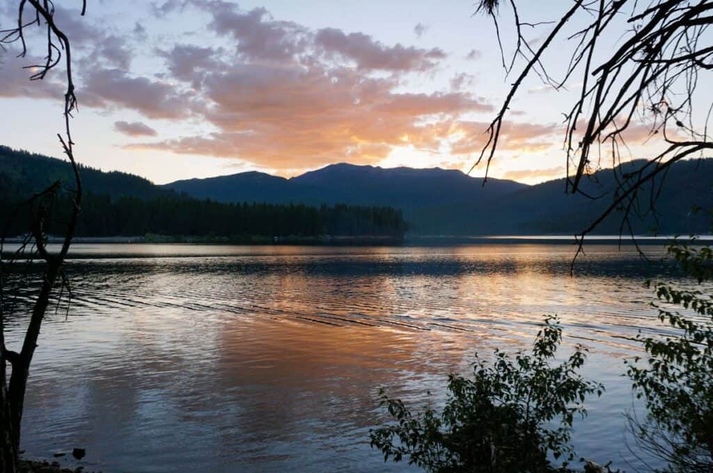 Pink clouds reflected on still lake water at sunset