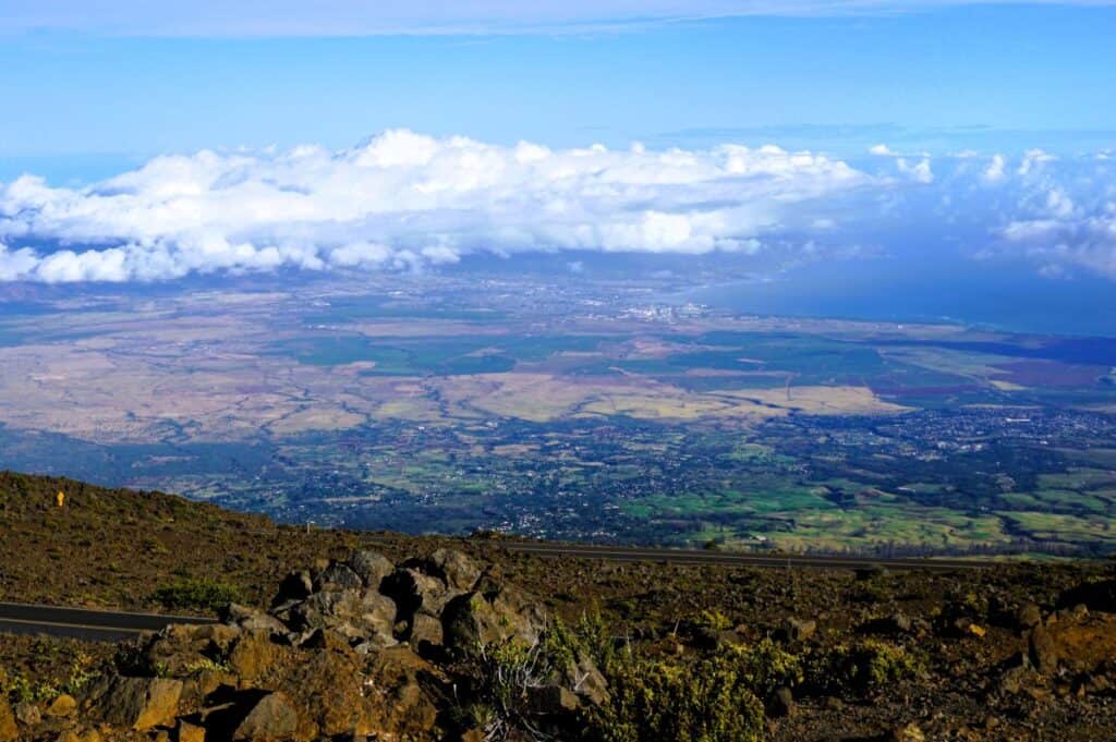 barren mountain top overlooking white clouds and a green patchwork landscape below