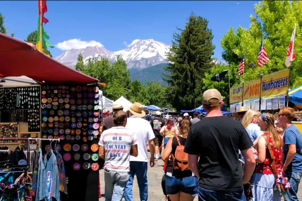 people walking through colourful market stalls on the 4th July with snowcapped Mount Shasta behind